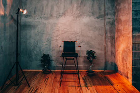 Single empty chair under a spotlight in a room on a stage, director chair, dark and moody toningの写真素材