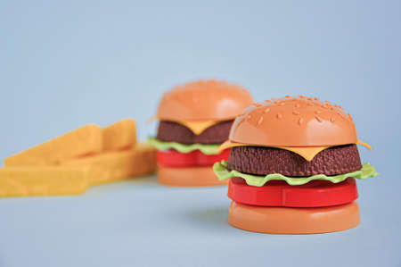 Plastic childrens toy burger with salad, tomato, meat and French fries on blue. Concept of harmful artificial food. unhealthy. Not organic. Not useful. Examining today's food industryの写真素材