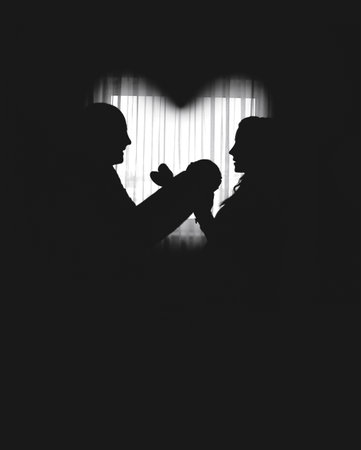 Silhouettes of happy parents, father and mother holding newborn baby by the window, heart shapedの写真素材