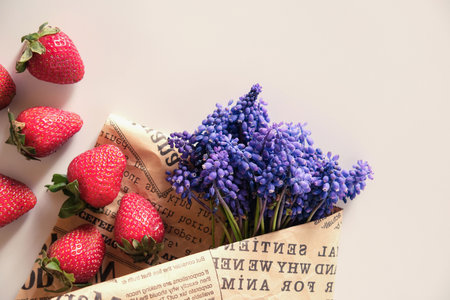 Red fresh strawberry and purple muscari flower with an vintage newspaper on white background, with copy space for textの写真素材