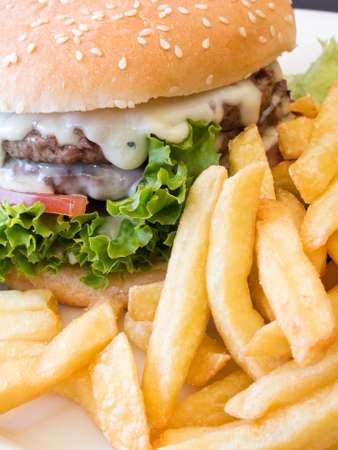 A delicious burger dripping with cheese together with crispy french friesの写真素材