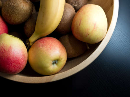 A trendy fruit bowl on dark background with apples, banana and kiwis