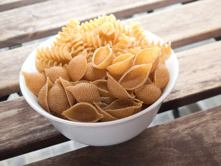A small white bowl with uncooked raw wholegrain pasta of two different kindsの写真素材