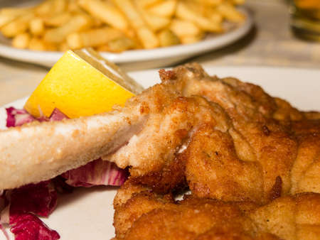 A closeup of a fried milanesa or Wiener Schnitzel with french fries and lemon