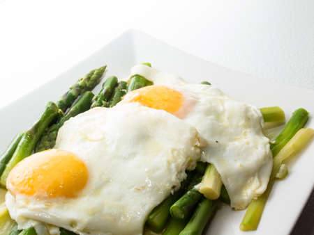 A plate with two fried eggs on a bed of asparagus vegetablesの写真素材