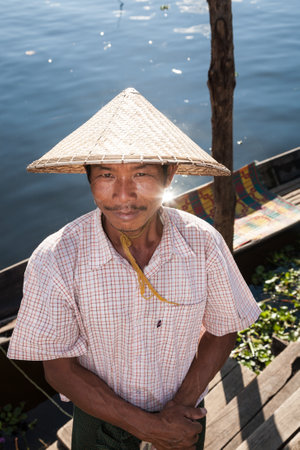 Maing Thauk, Myanmar - 2017, January 4 : A boatman with a conical straw hat on the Inle Lake looking up at the camera in front of water and boatのeditorial素材