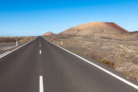 A road in Lanzarote cutting through a volcanic desert area with the Montana Colorada on the right, Canary Islands, Spainの写真素材