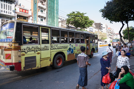 Yangon, Myanmar - 2017, January 8 : An urban scene with a public bus covered with advertisements and people on the street, Yangon, Burmaのeditorial素材
