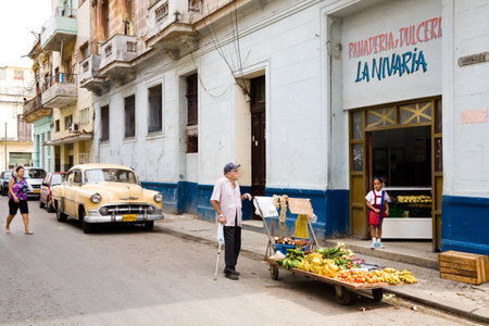 Havana, Cuba - November 28, 2012 : An urban street scene in the area of Havana called Centro in the Calle Virtudes with fruit cart, bakery, a classic american car and cubansのeditorial素材