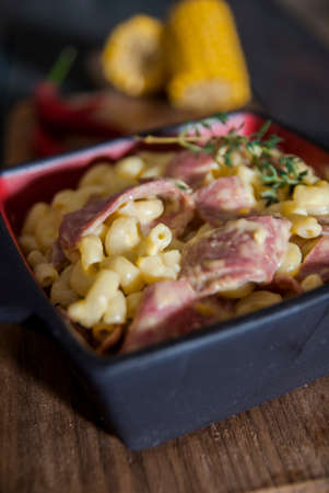 Twisted Mac and Cheese with Ham on a Wooden Cutting Board. Red Hot Chili Peppers and Corn on the...