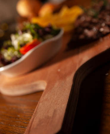 Grilled Filet of Beef with French Fries and Green Salad on a Wooden Plate. Ketchup and Barbecue Sauce, Christmas Gift Basket, Bread in a Wooden Basket at Backgroundの写真素材
