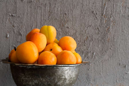 Apricots in a Vintage Bowl with Cinnamon Sticks and Leaves on a Gray Concrete Background