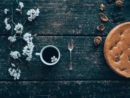 Mug of coffee and homemade cake with nuts and chocolate on old wooden Board and flowering branches of peach in springtime.の写真素材