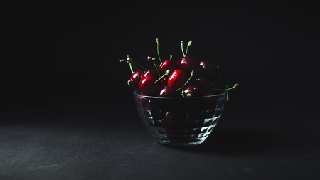Cherries in a transparent plate on a black backgroundの写真素材