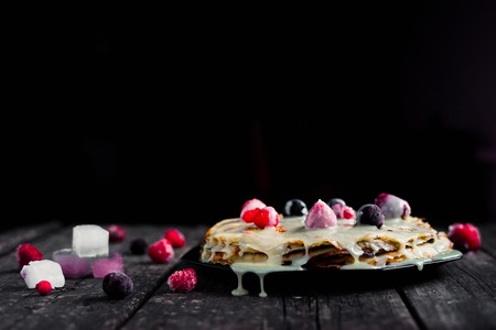 Homemade pancakes with flowing condensed milk sauce served on plate with strawberry and cherry with ice cream on vintage wood tableの写真素材