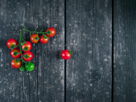 Bunch of fresh ripe Cherry tomatoes with sea salt on black wooden chopping board over black textured background. Top view.の写真素材