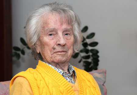 Happy woman, 98 years old, sits in the armchair in the room 