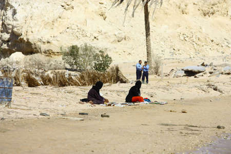 SHARM EL-SHEIKH, EGYPT, OCTOBER 25: Poor Arabian women wearing a black head covering sit on the sand beach and police in the background near the luxury hotelのeditorial素材