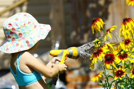 Little girl in summer hat watering yellow flowersの写真素材