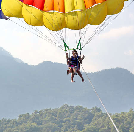 KEMER, TURKEY - AUGUST 18, 2015: Parasailing in a blue sky near sea beach. Parasailing is a popular recreational activity among tourists in Turkey.のeditorial素材