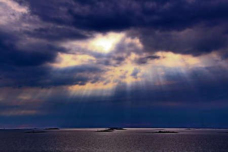 The sun behind the clouds with rays of light shining down on seaの写真素材