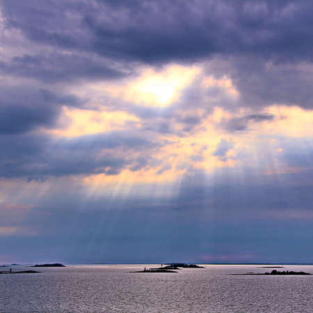 The sun behind the clouds with rays of light shining down on sea