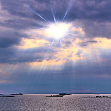 The sun behind the clouds with rays of light shining down on seaの写真素材