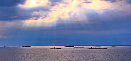 The sun behind the clouds with rays of light shining down on seaの写真素材