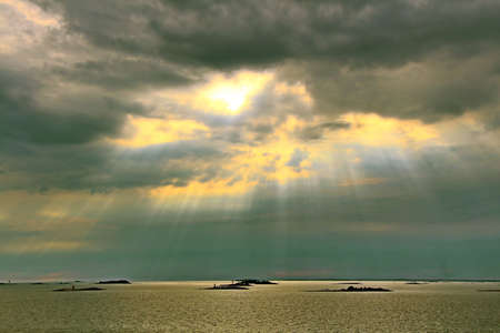 The sun behind the clouds with rays of light shining down on seaの写真素材