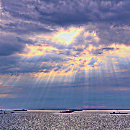 The sun behind the clouds with rays of light shining down on seaの写真素材