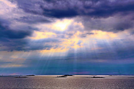The sun behind the clouds with rays of light shining down on seaの写真素材