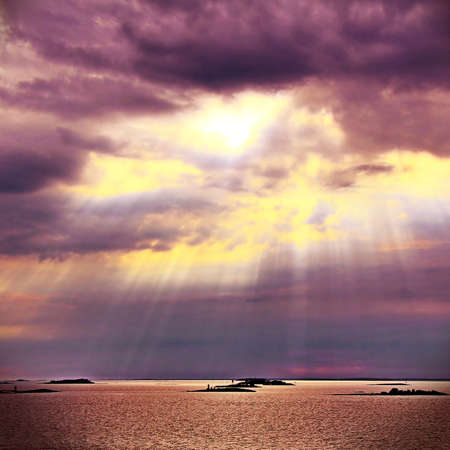 The sun behind the clouds with rays of light shining down on seaの写真素材