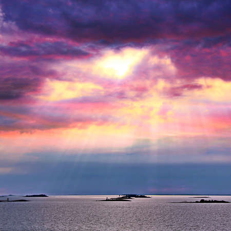 The sun behind the clouds with rays of light shining down on seaの写真素材