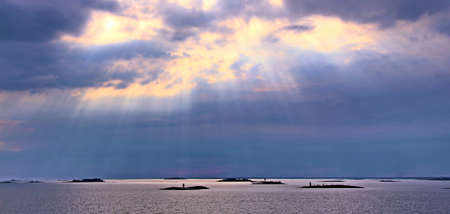 The sun behind the clouds with rays of light shining down on seaの写真素材