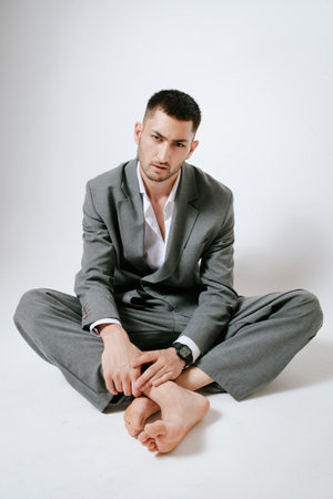Handsome man in gray suit sits on the floor barefootの写真素材