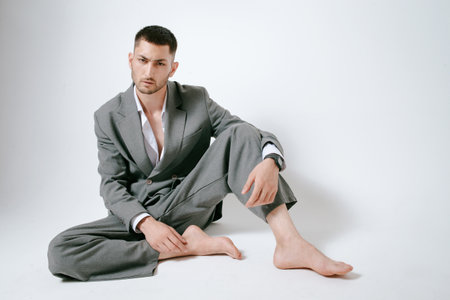 Handsome man in gray suit sits on the floor barefootの写真素材