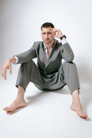 Handsome man in gray suit sits on the floor barefootの写真素材