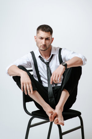 A man with white shirt and tie sits on a chair in studio.の写真素材