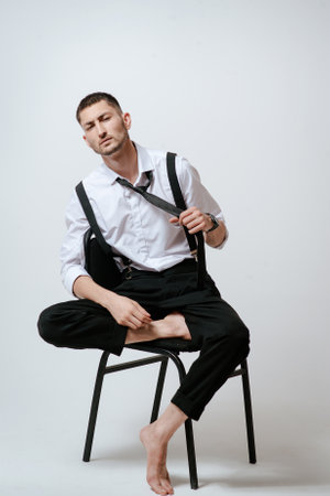 A man with white shirt and tie sits on a chair in studio.の写真素材