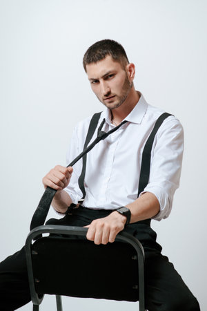 A man with white shirt and tie sits on a chair in studio.の写真素材