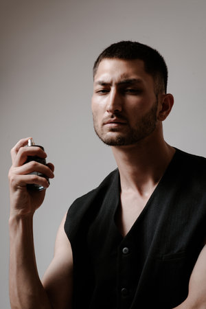 The handsome man uses perfume. Bottle of perfume in a man`s hand. fashion model
