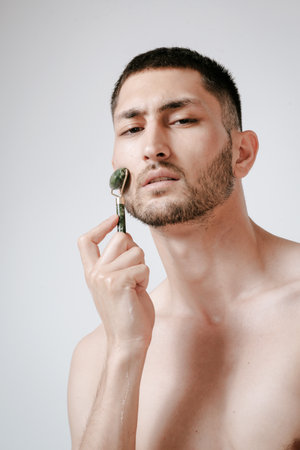 A handsome young man in a wellness center uses a jade guasha roller on his face , highlighting beauty and relaxation in an spa settingの写真素材