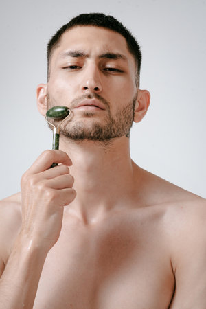 A handsome young man in a wellness center uses a jade guasha roller on his face , highlighting beauty and relaxation in an spa settingの写真素材