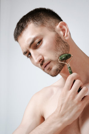 A handsome young man in a wellness center uses a jade guasha roller on his face , highlighting beauty and relaxation in an spa settingの写真素材