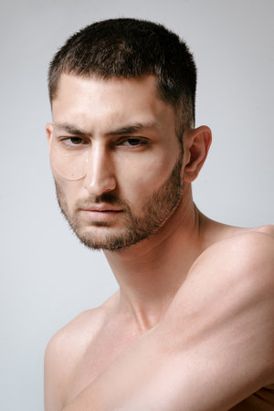 Man facial care skin rejuvenation face eye patches. Man facial care. Skin rejuvenation. Cosmetic product advertising. Satisfied caucasian guy applying collagen gel face eye patches on gray background.の写真素材