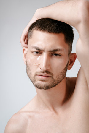 Man facial care skin rejuvenation face eye patches. Man facial care. Skin rejuvenation. Cosmetic product advertising. Satisfied caucasian guy applying collagen gel face eye patches on gray background.の写真素材