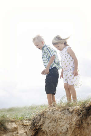 Brother and sister looking over the edge of a sand dune.の写真素材