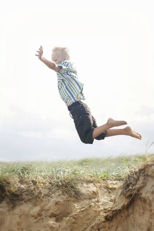 Boy jumping of sand dune at the beach.の写真素材