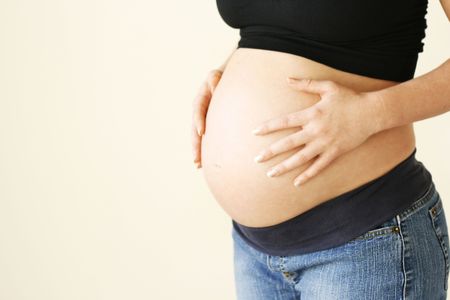 Woman holding her pregnant belly against a light background.の写真素材