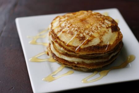 A stack of delicious golden pancakes with honey on a white plate.の写真素材